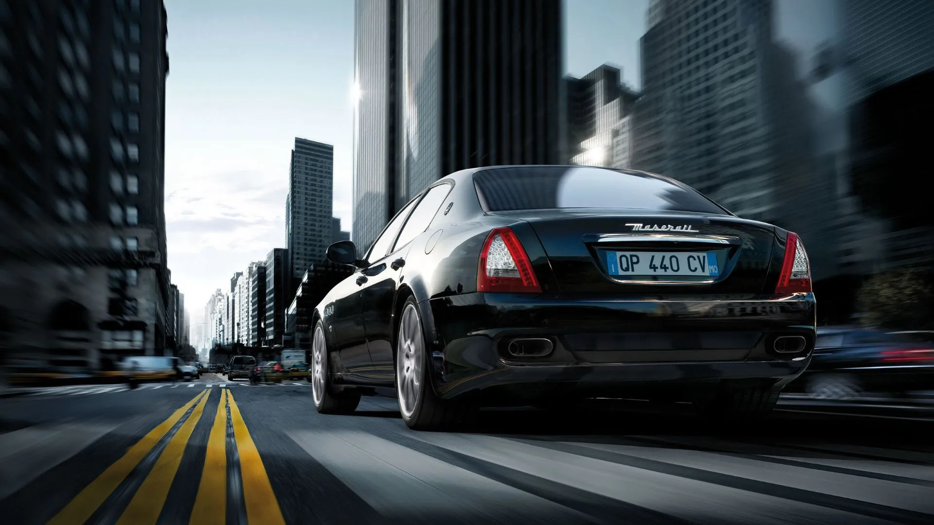 Ảnh 3/4 phía sau Maserati Quattroporte 2008 màu đen đang chạy trên phố, nhấn vào dáng xe năng động.